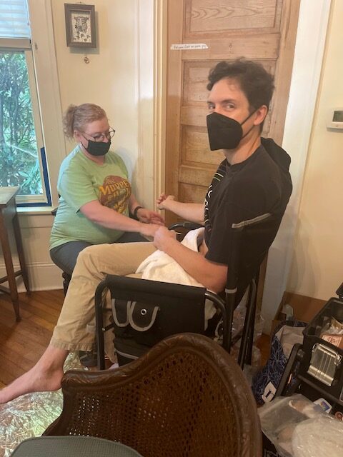 Chris Malco looks at the camera, wearing a mask as the special effects artist applies makeup to his arm.